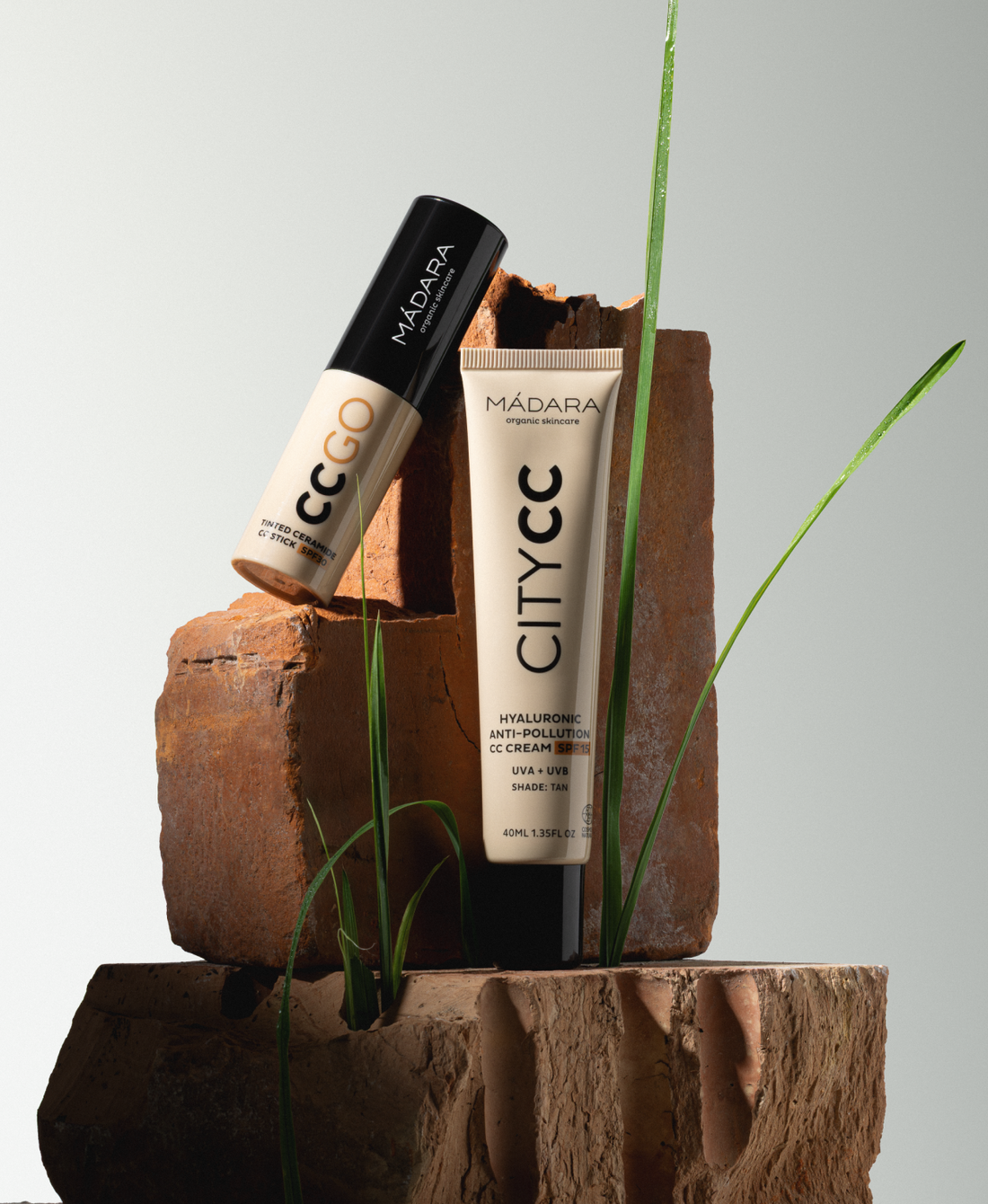 MÁDARA City CC cream and CC Go tinted stick displayed on stacked clay blocks with green grass accents against a clean background
