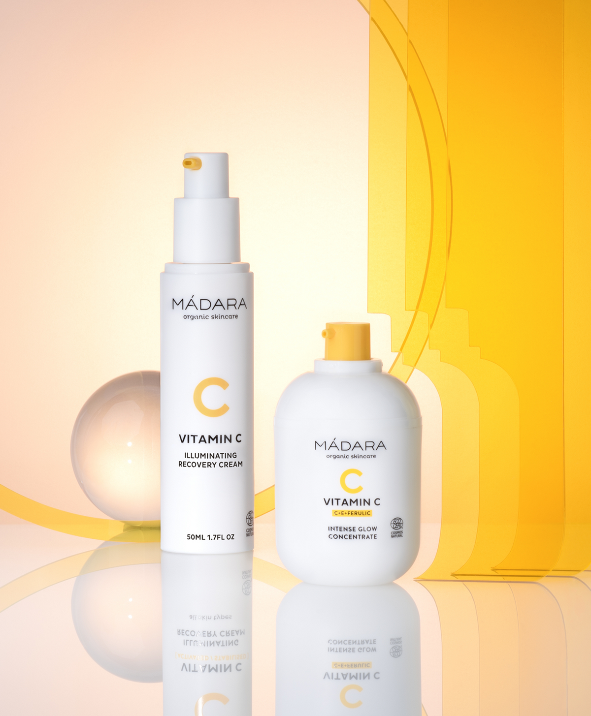 Madara Vitamin C collection with Intense Glow Concentrate and Illuminating Recovery Cream on a reflective surface with a yellow background