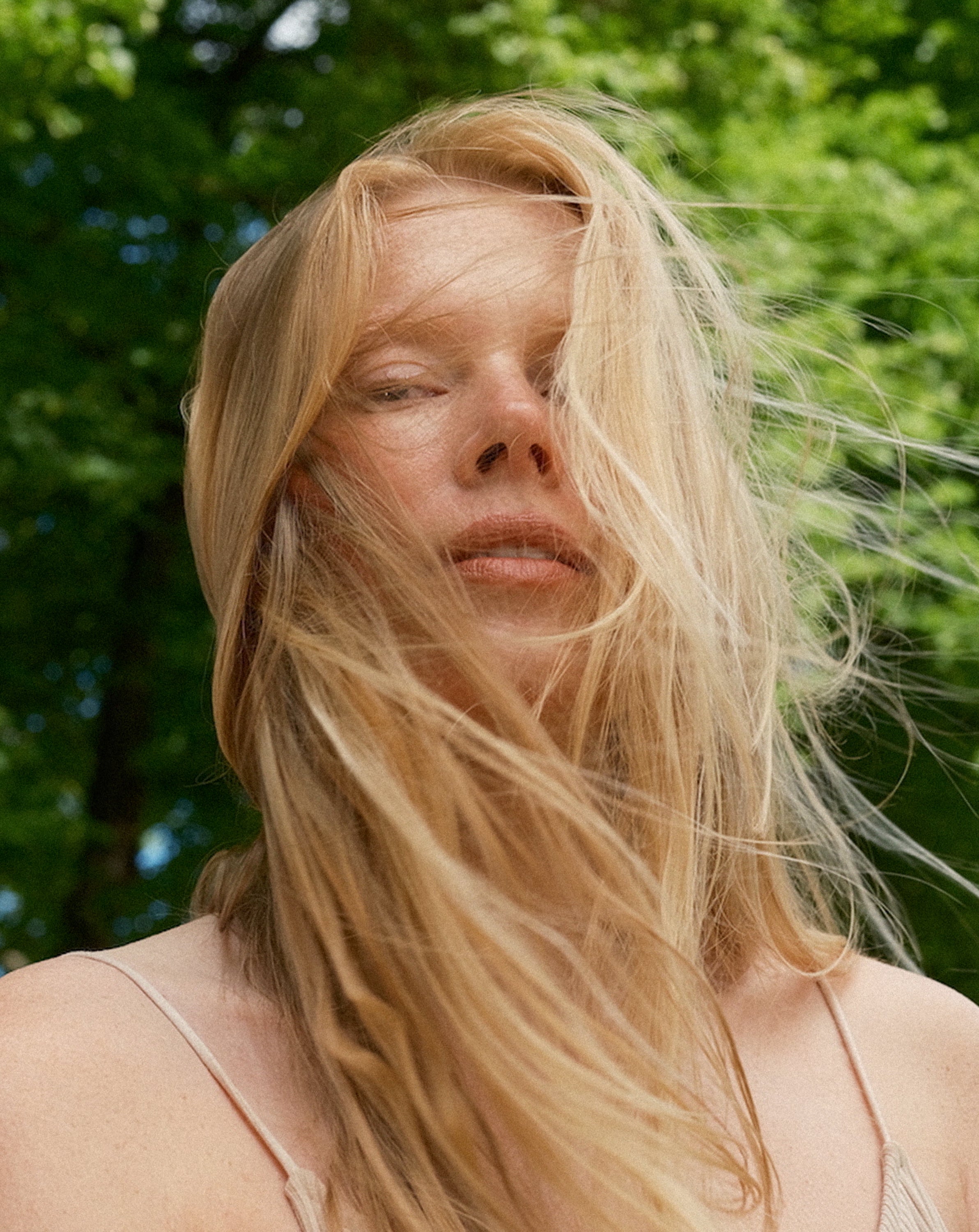 Woman with long blonde hair in a natural setting with greenery