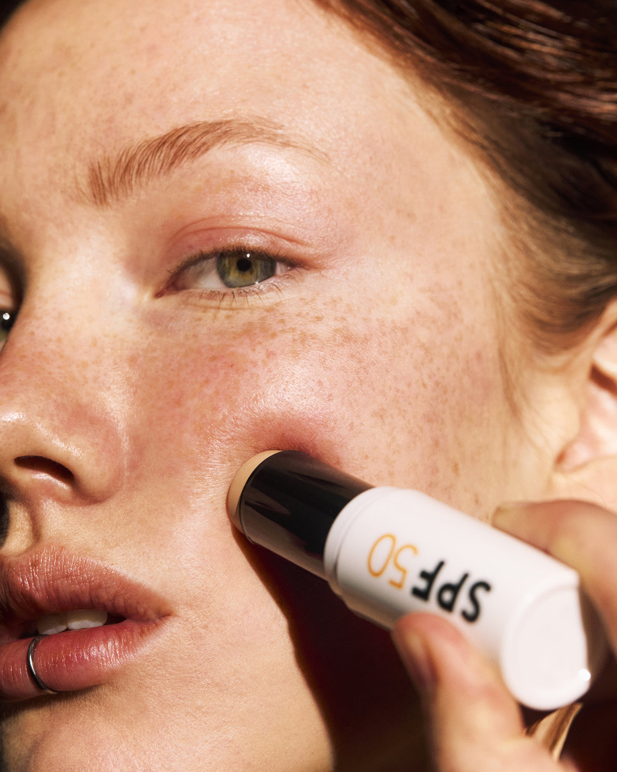 Person applying MADARA SPF 50 sunscreen stick to face