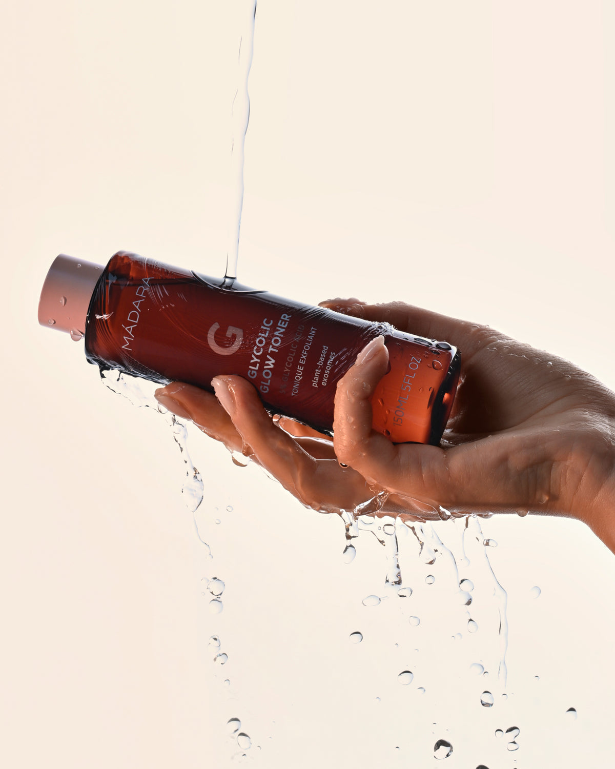 Hand holding a bottle of exfoliating MADARA Glycolic Glow Toner with water droplets around it 