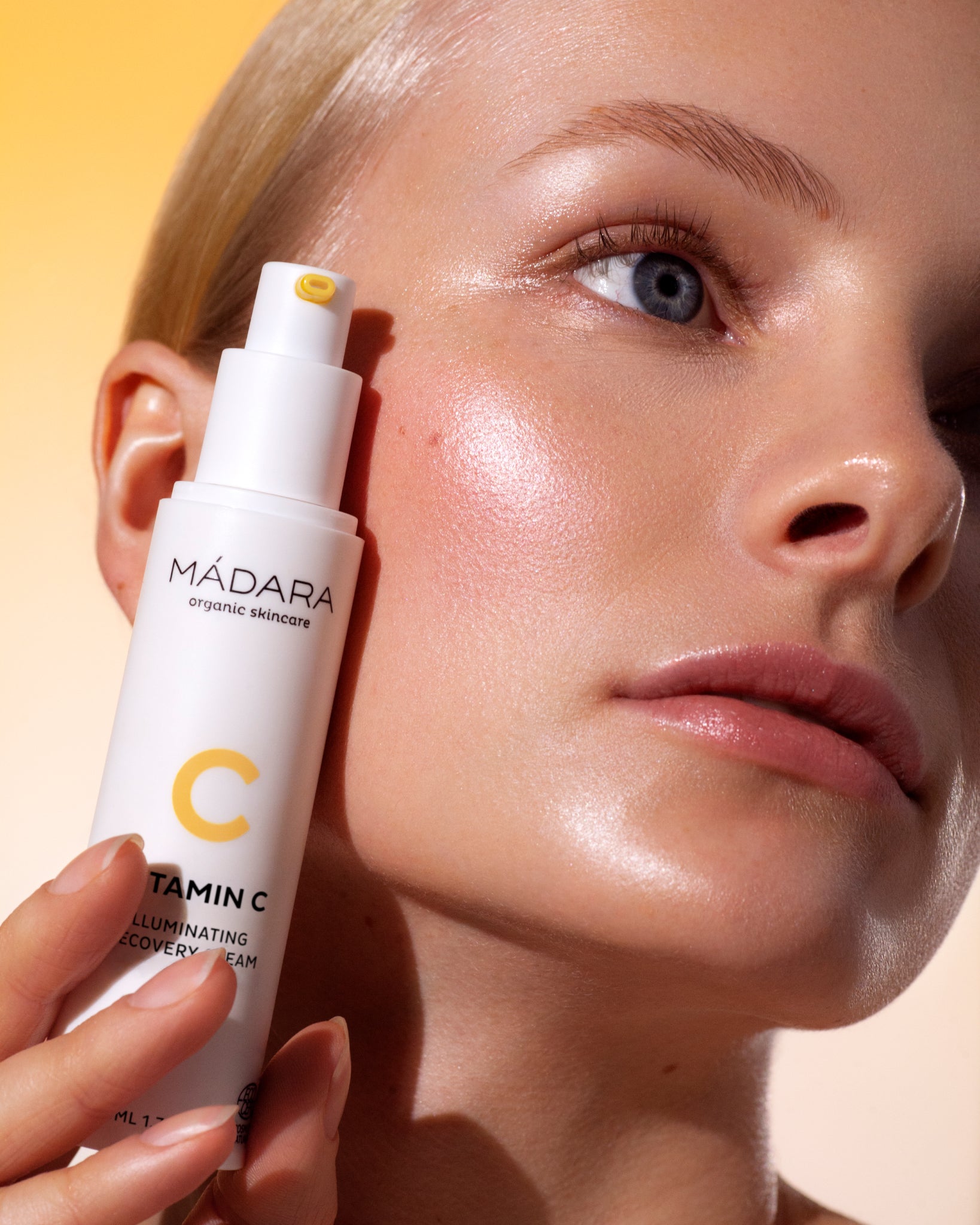 Person holding a Madara Vitamin C product close to their face against a yellow background