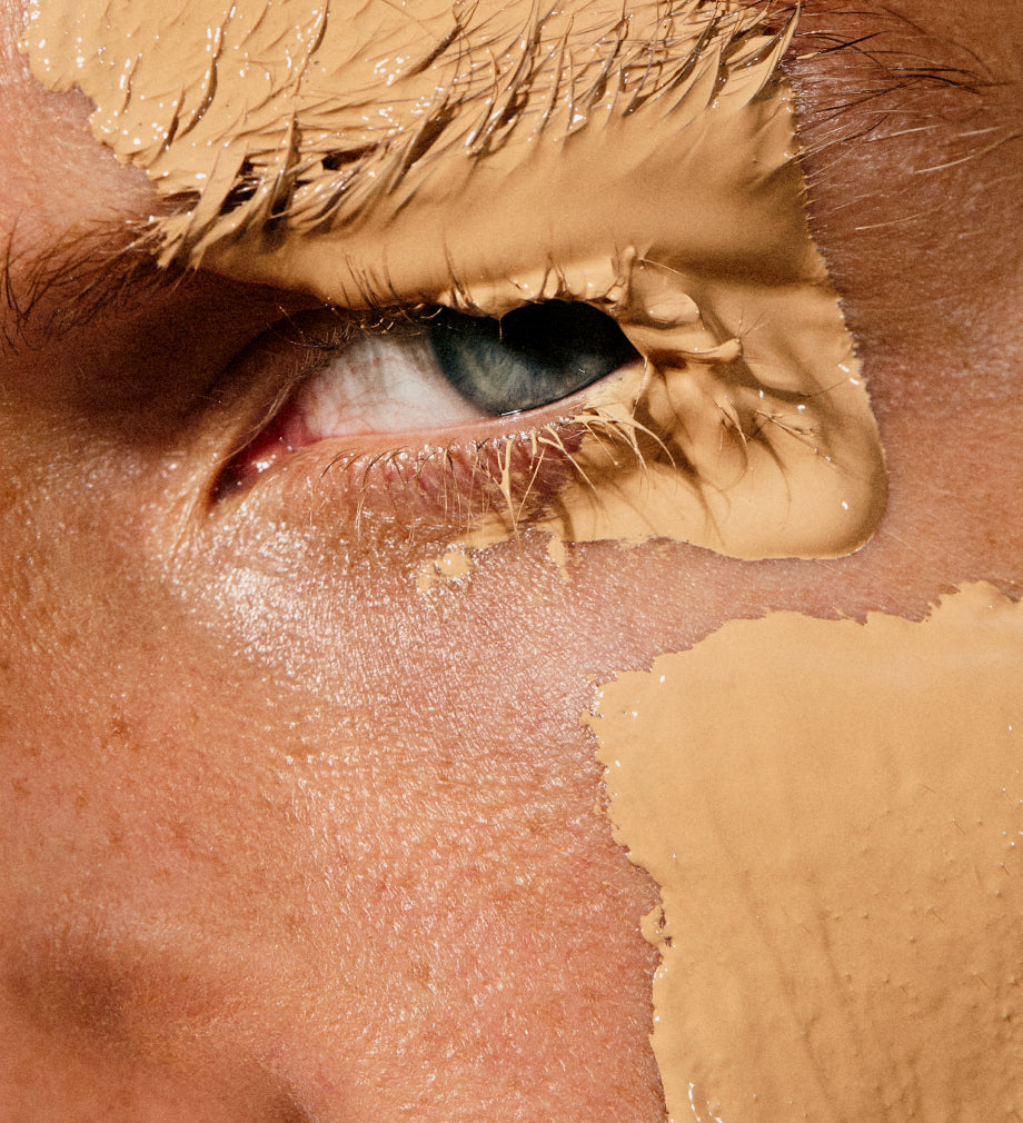 Close-up of an eye and skin with beige foundation applied in expressive strokes