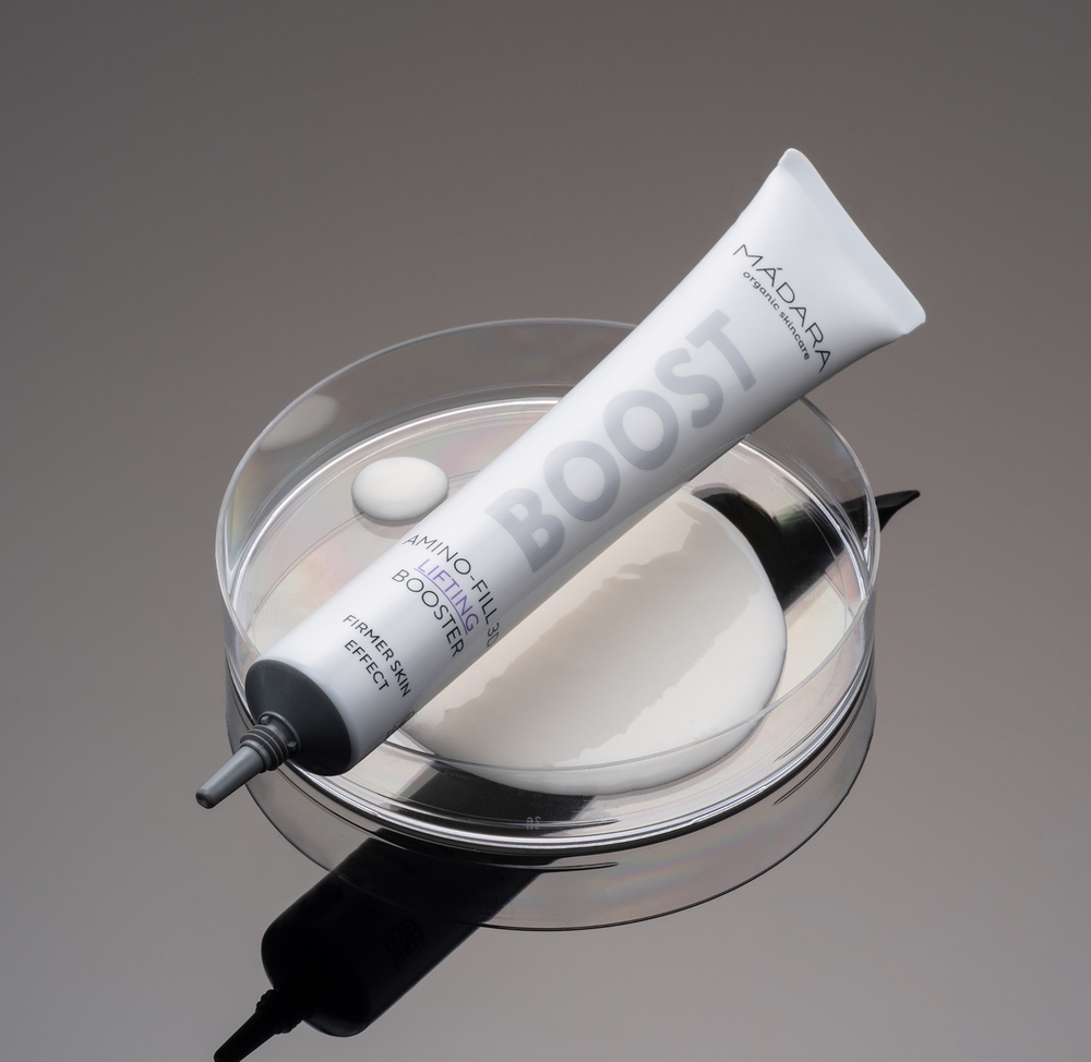 MÁDARA BOOST Amino-Fill 3D Lifting Booster tube displayed on a laboratory petri dish with skincare formula, highlighting a science-inspired approach to firming and lifting skincare