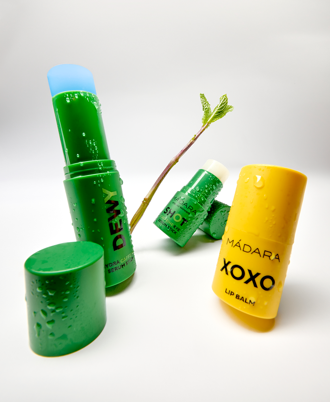 MÁDARA DEWY serum stick, SHOT caffeine eye serum stick and XOXO lip balm with water droplets and green botanical stem