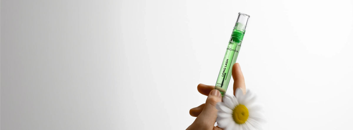 MÁDARA Long Lash peptide serum held in hand beside a white flower