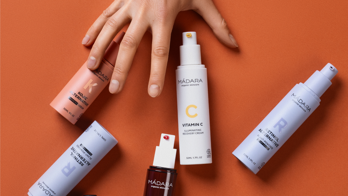 MÁDARA skincare products arranged on an orange background, featuring Vitamin C, Retinol Alternative and Kojic Alternative formulas