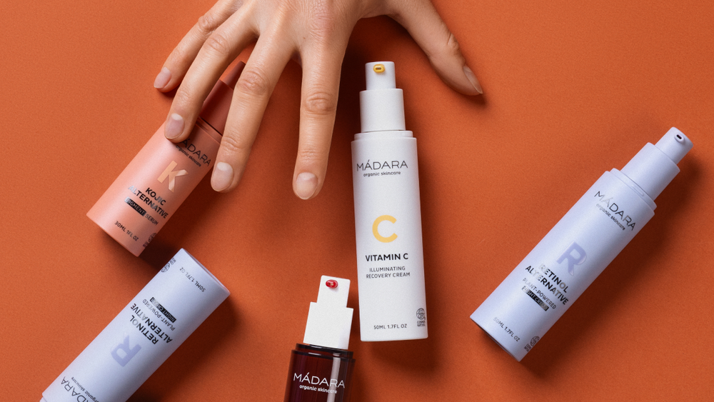 MÁDARA targeted skincare products displayed on an orange background with a hand reaching toward them 