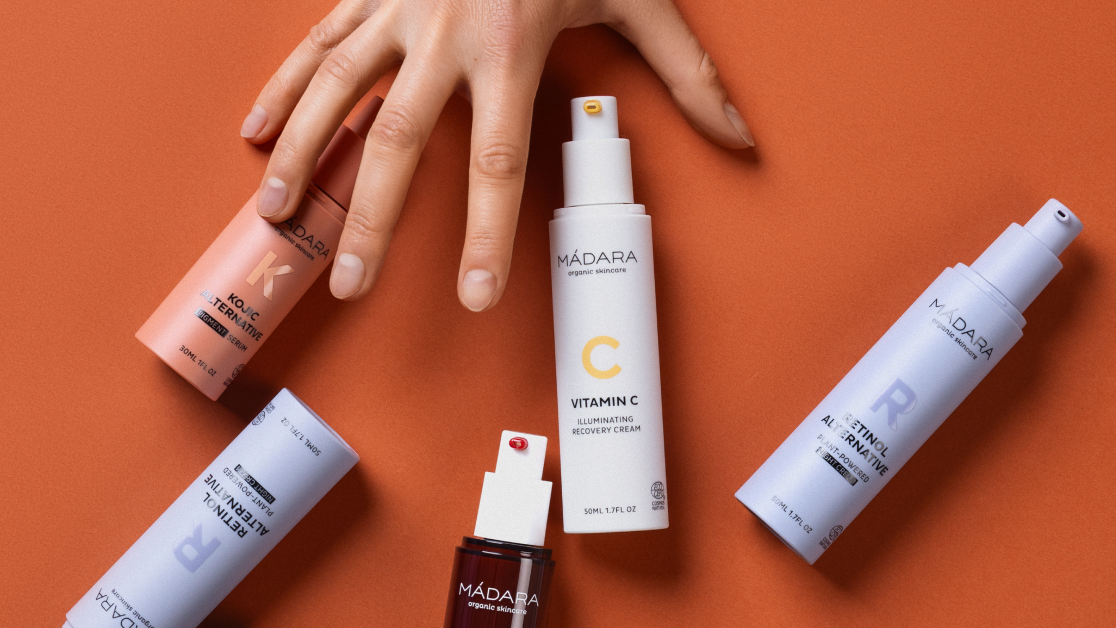 MÁDARA targeted skincare products displayed on an orange background with a hand reaching toward them 