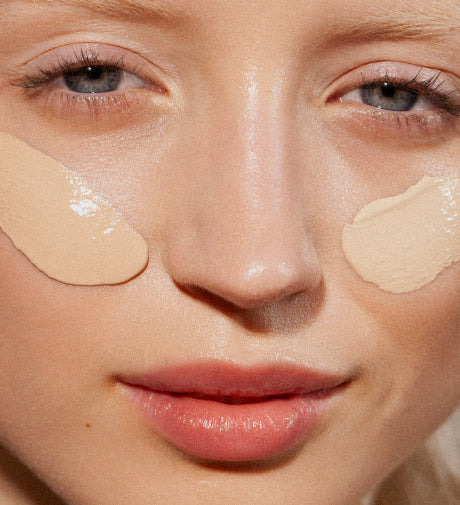 Close-up of a woman with beige foundation swatches applied to both cheeks