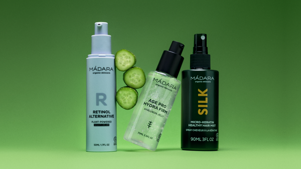Three MÁDARA organic skincare products on a green background Retinol Alternative night cream, Age Pro Hydra Firm hyaluron jelly, and Silk Micro-Keratin Healthy Hair Mist, with sliced cucumber