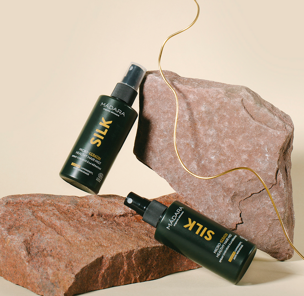 Two MÁDARA Silk Micro-Keratin Healthy Hair Mist bottles arranged on natural stones