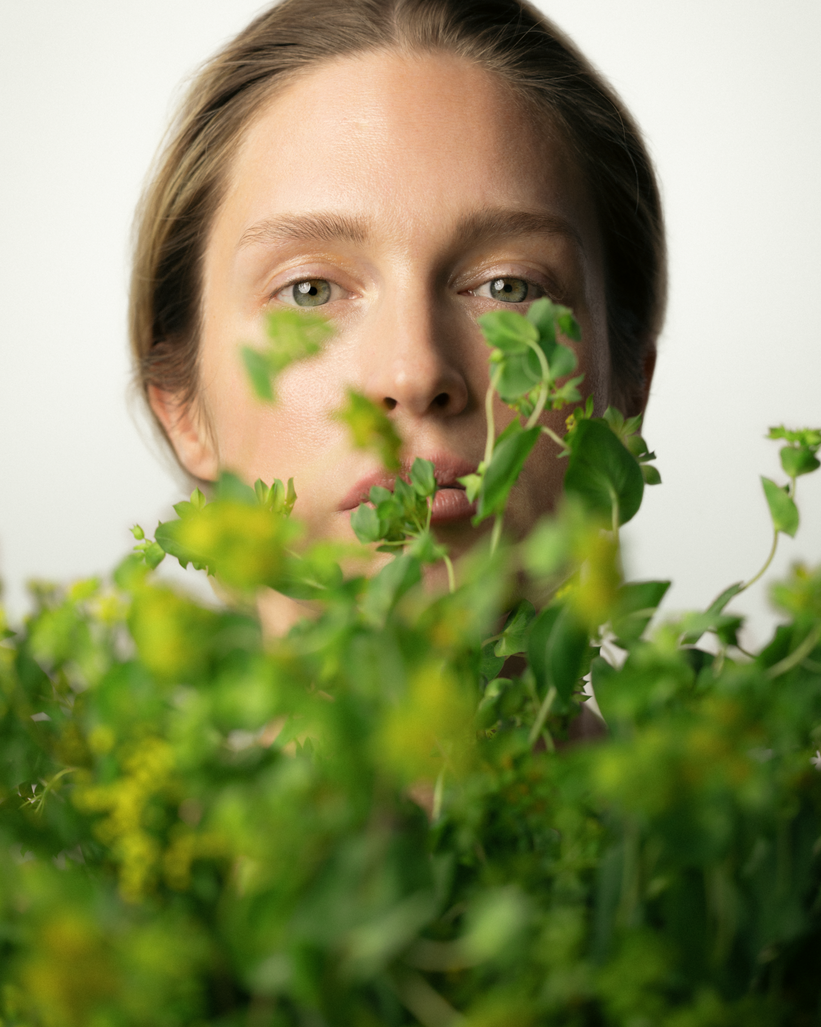 Person with green leaves in front of their face on a white background