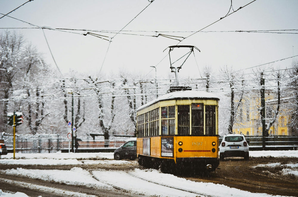 A vintage tram navigates snowy streets in Milan, Italy, highlighting winter transportation