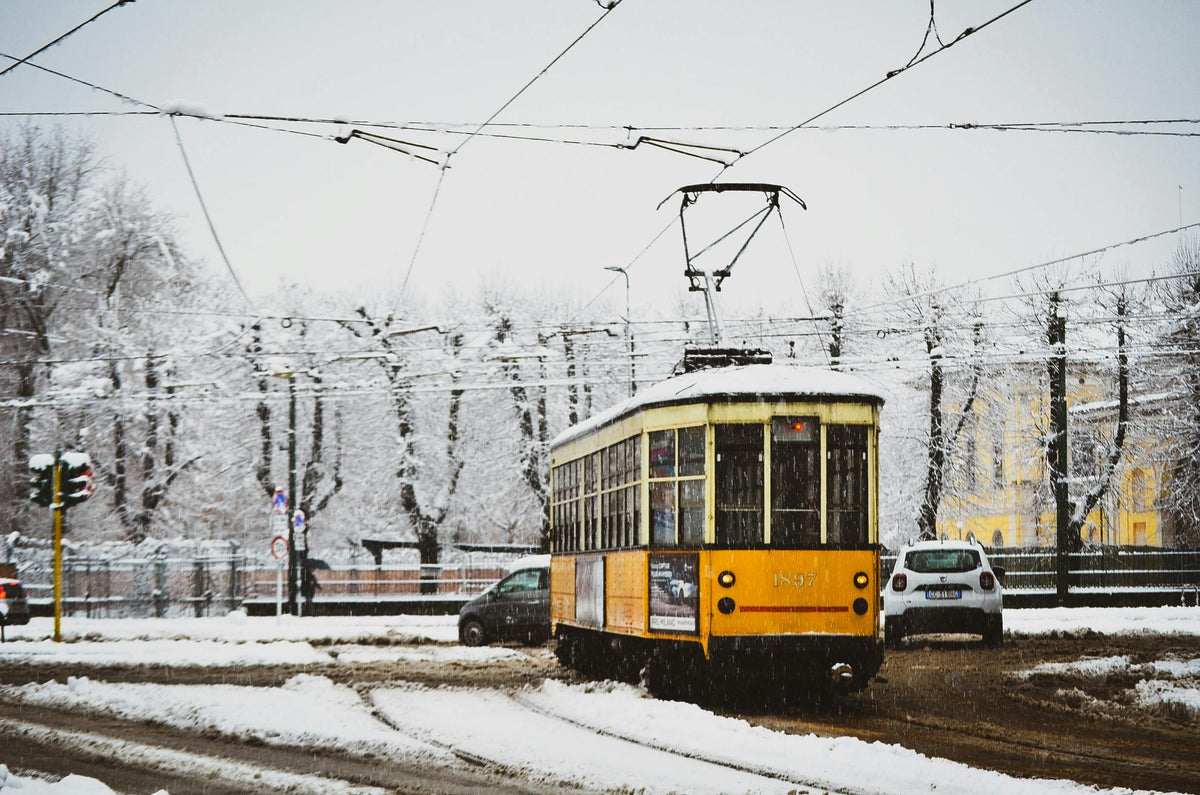 A vintage tram navigates snowy streets in Milan, Italy, highlighting winter transportation