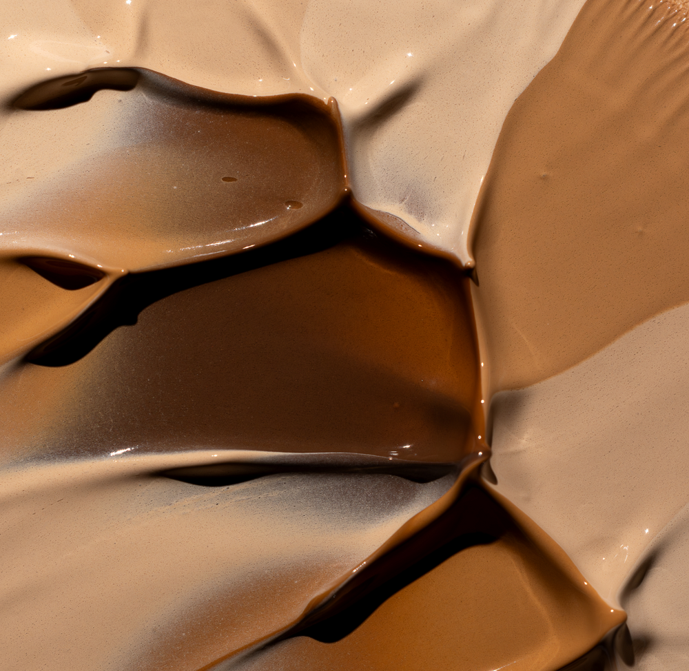 Close-up of multiple creamy foundation swatches in light to deep shades blended together with glossy, smooth texture, showcasing the shade range of MÁDARA Cosmetics Skin Equal Soft Glow Foundation SPF20
